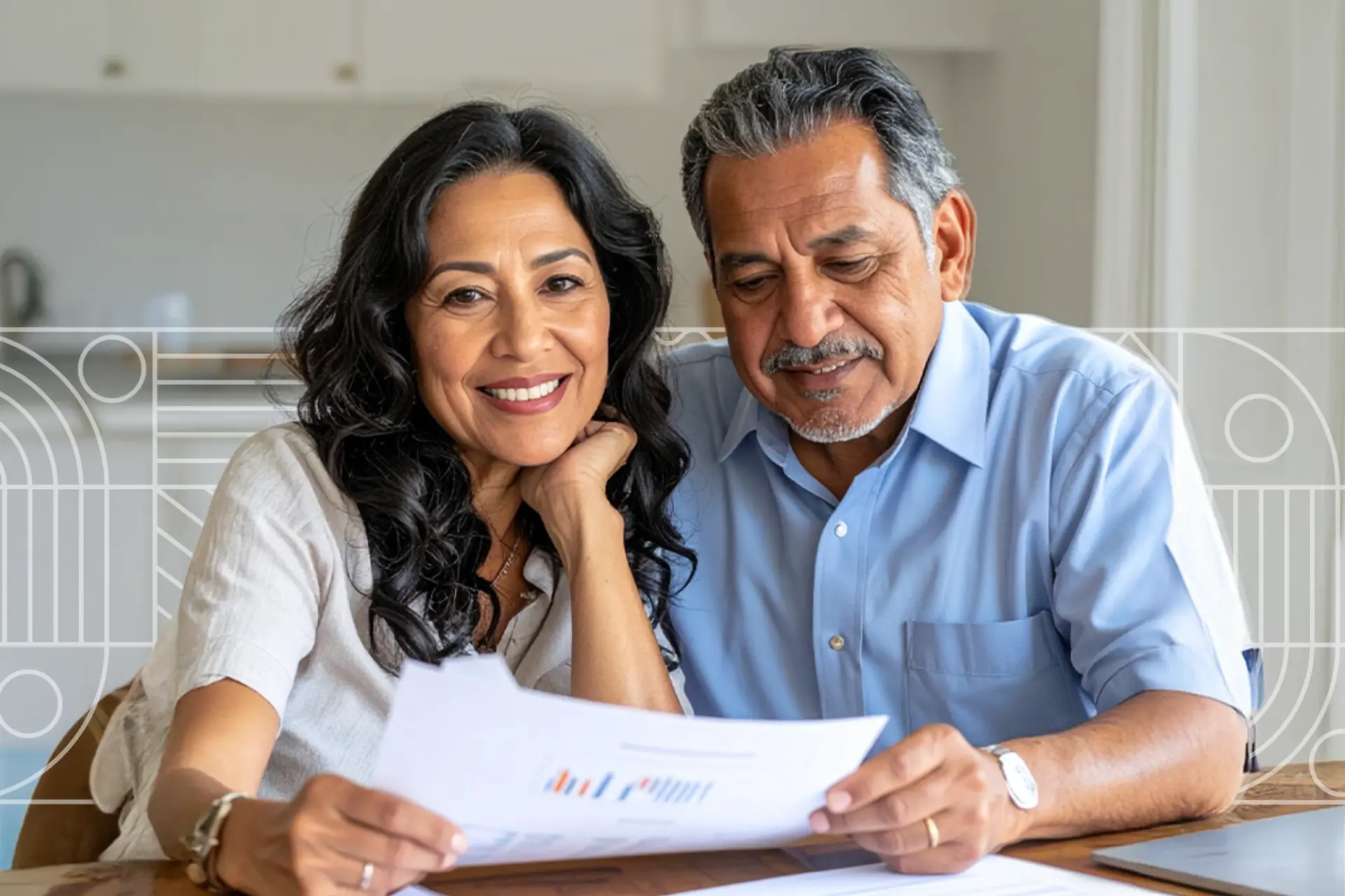 Pareja de mediana edad en cocina moderna, mujer sonriendo a cámara y hombre revisando un documento; mesa con hojas y fondo desenfocado con patrones geométricos sutiles.